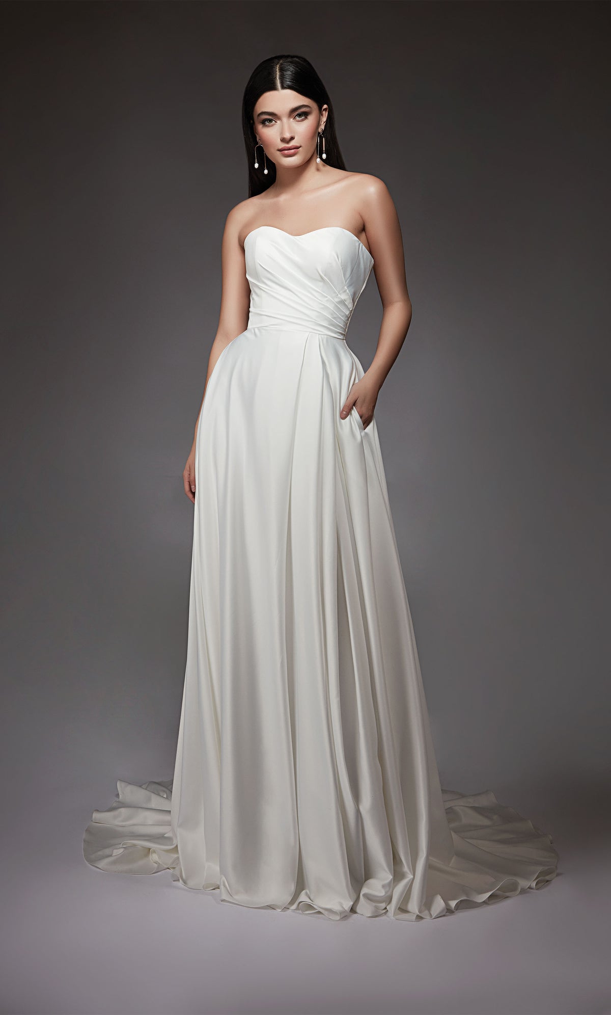 A-line satin bridal gown featuring a strapless, semi-sweetheart neckline, a pleated bodice, and high side slit. Satin covered buttons cascade down the back of the dress from the top to the end of the elegant train.