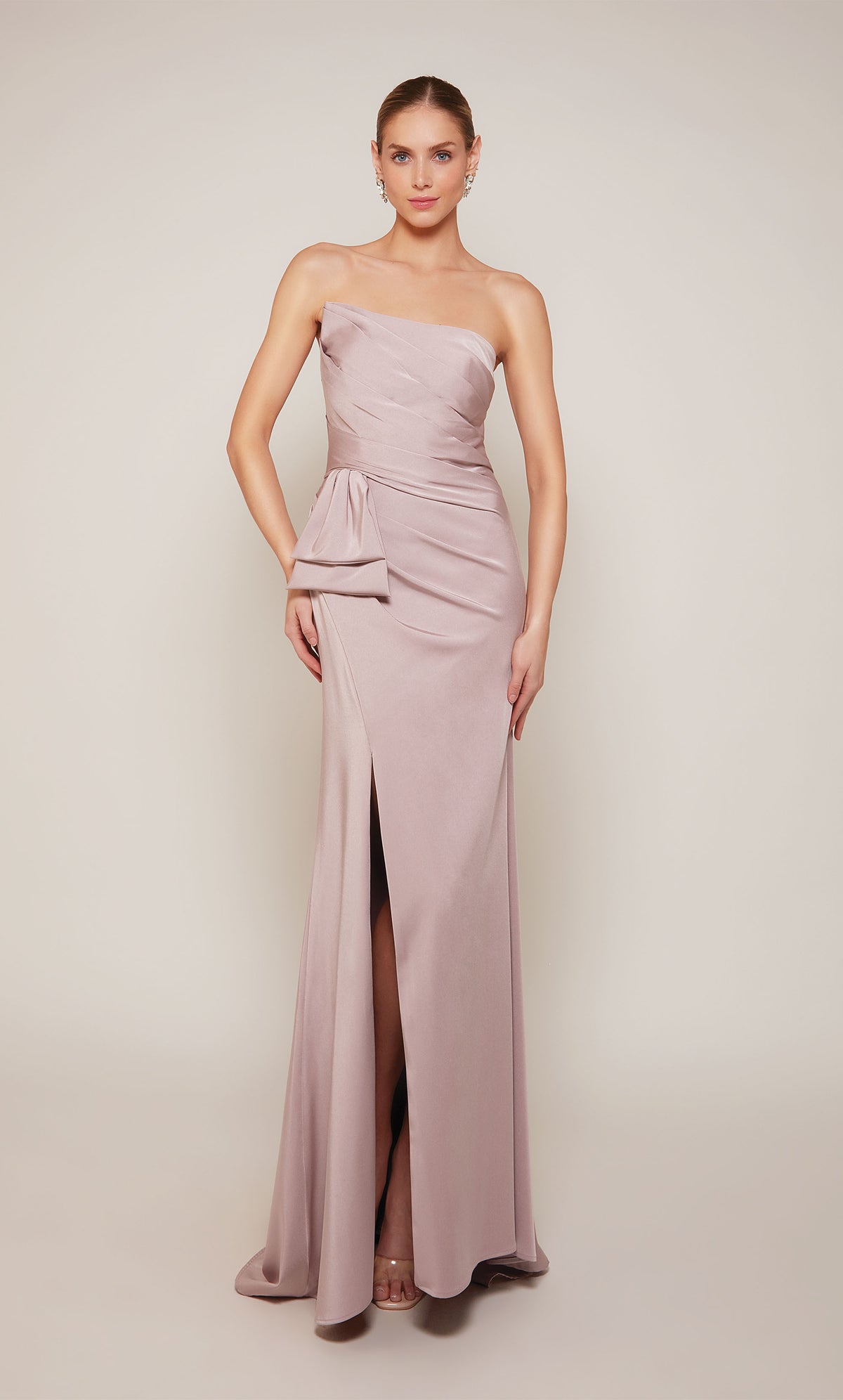 A strapless designer gown highlighting a pleated bodice, a bow at the waistline, and a side slit in the color rosewood.