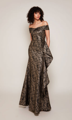 A black and gold Jacquard formal gown with an off the shoulder, twist neckline and a cascading side ruffle.