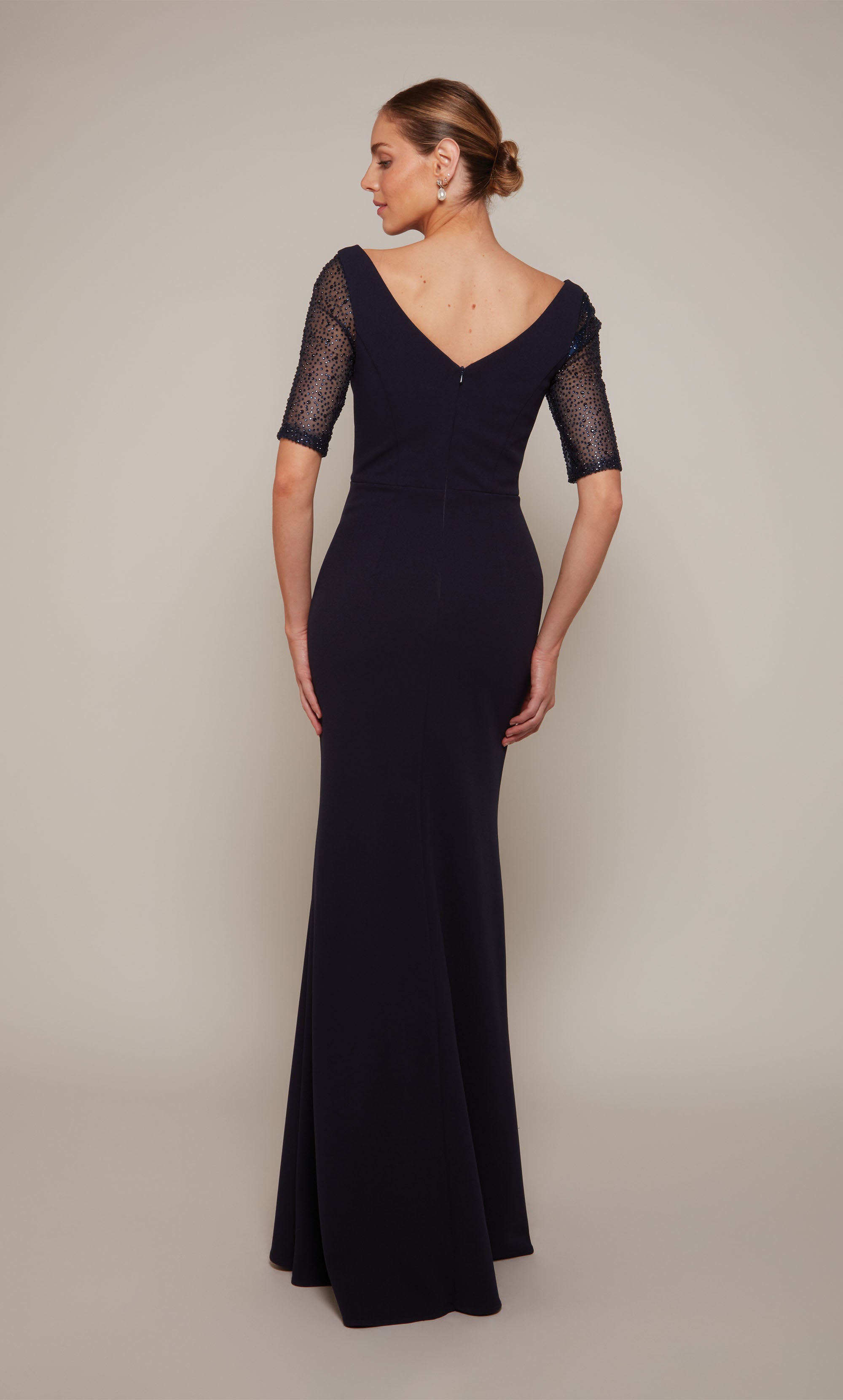 A long navy wedding guest dress with a wide V-neckline, short embellished sleeves, and a fitted skirt that flares slightly from the knee to the bottom of the hemline.