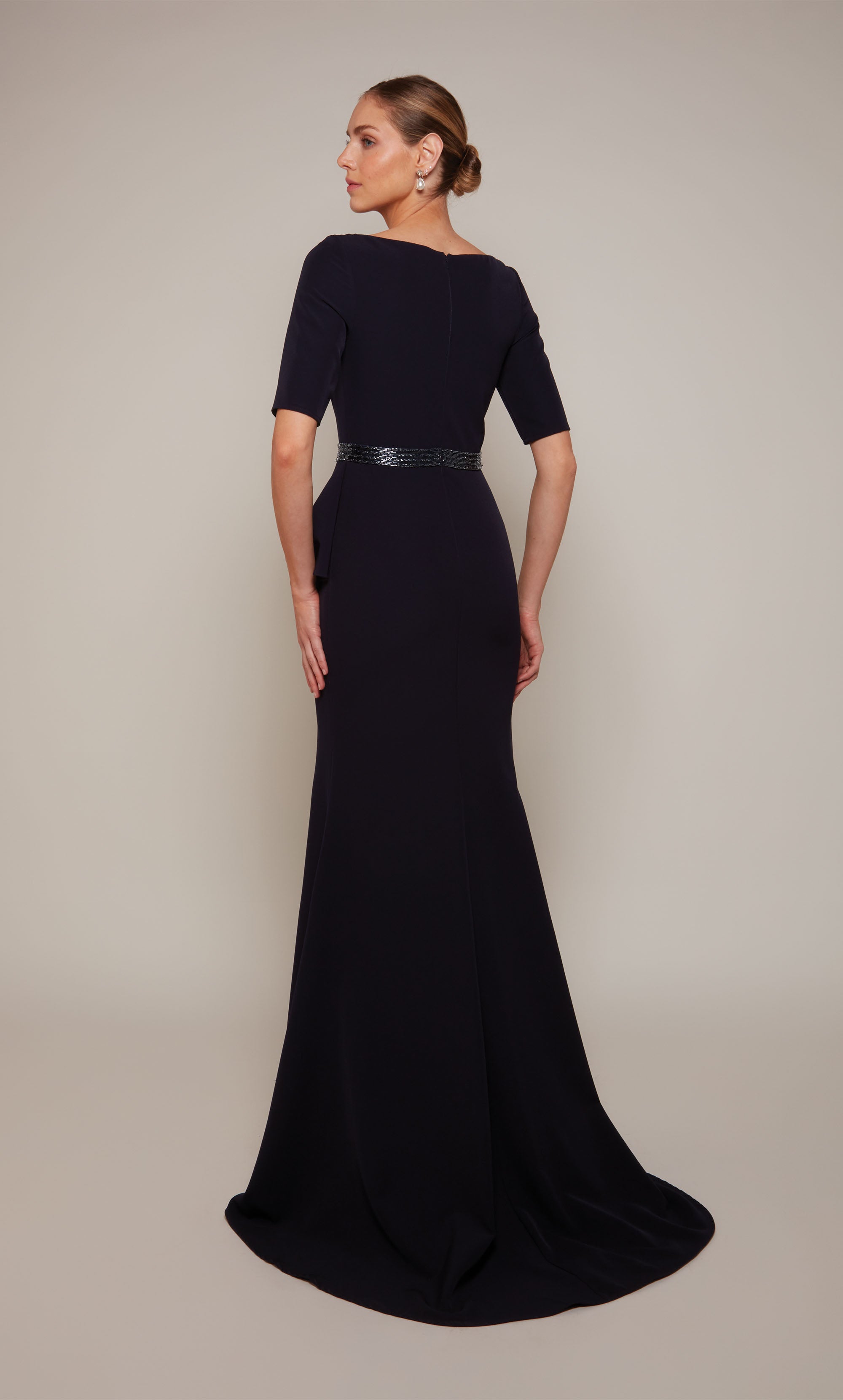 A navy scooped neck designer gown with a peplum short sleeve bodice, a beaded waistline, a side ruffle, and side slit.