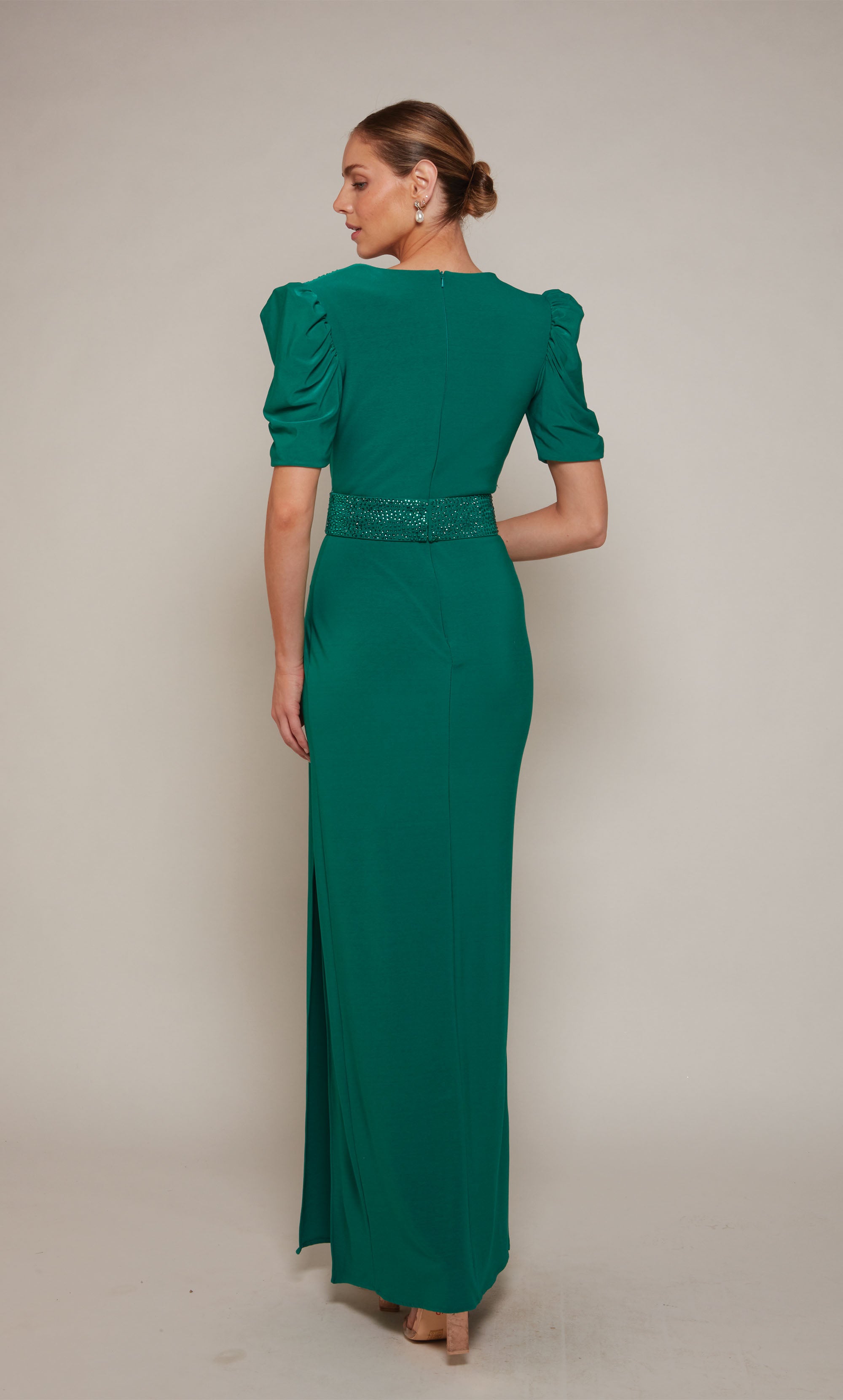 An emerald evening gown with puff sleeves, a V-neckline, an embellished belt, and elegant side slit.