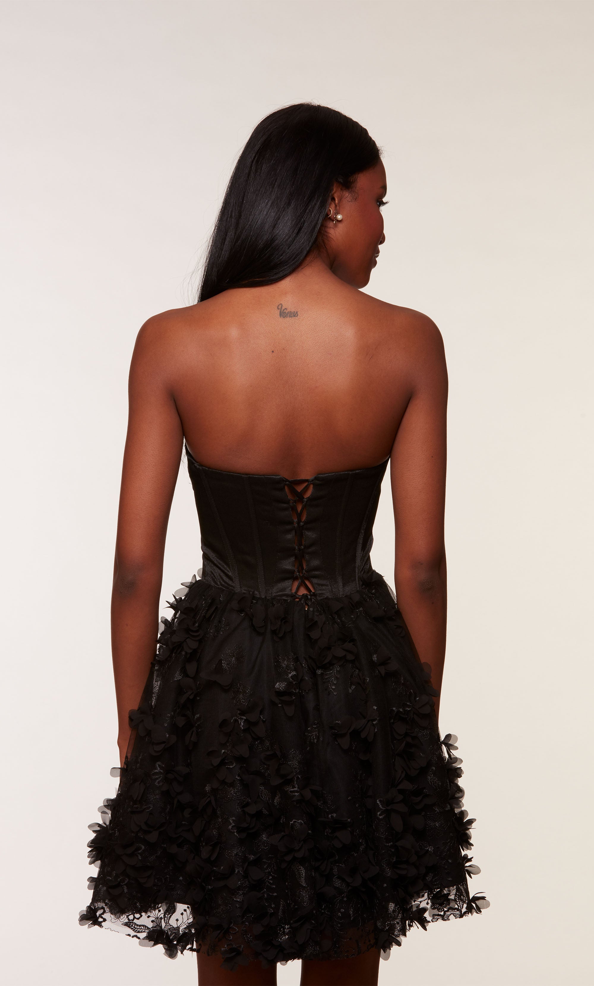 A black strapless satin corset dress, showcasing a fitted bodice and a flared skirt adorned with intricte 3D flowers.