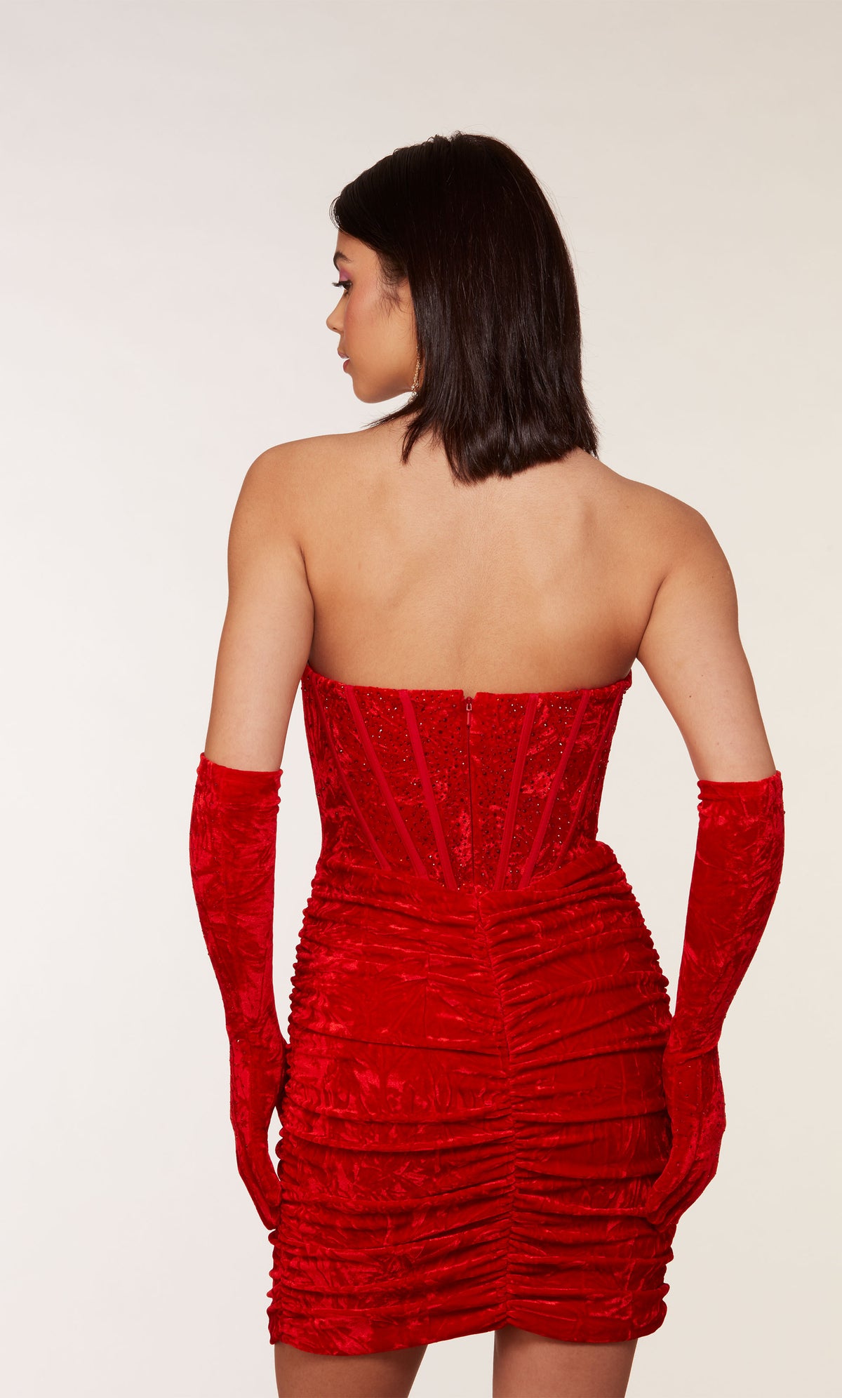 An 80&#39;s inspired red velvet corset dress with a strapless neckline and a ruched skirt. The matching gloves level up this chic look.