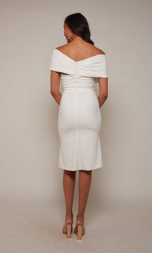 A chic, knee length cocktail dress with an off the shoulder neckline, ruching detail, and a closed zipper back in ivory.