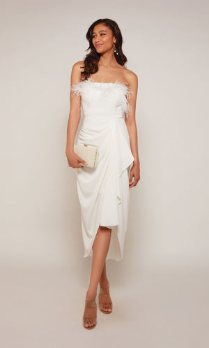 An ivory colored asymmetrical hemline dress  with a strapless neckline, feather trim, and a cascading drape in the front.