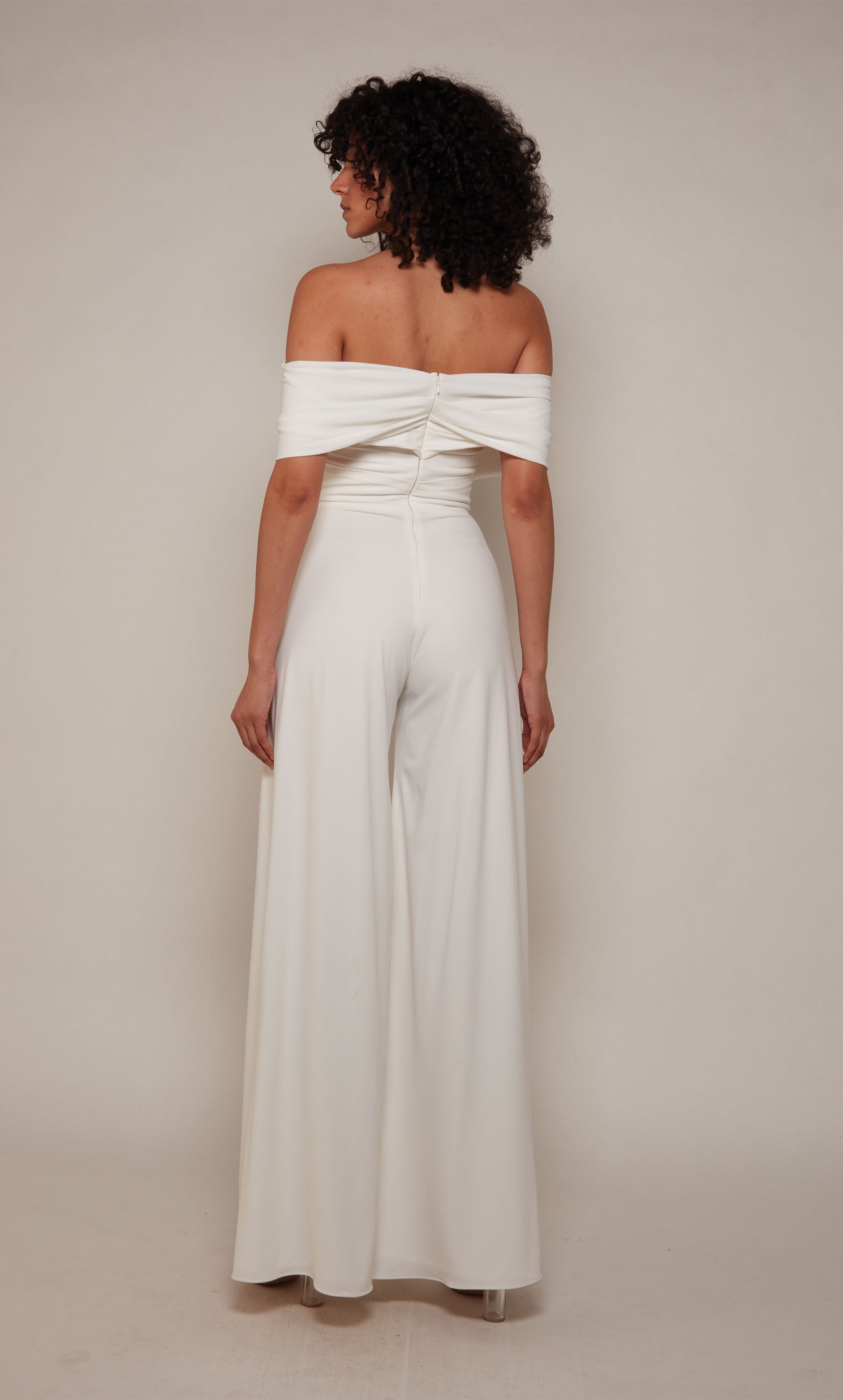 An off-the-shoulder jumpsuit with a wide fit and flare pant in white satin fabric.