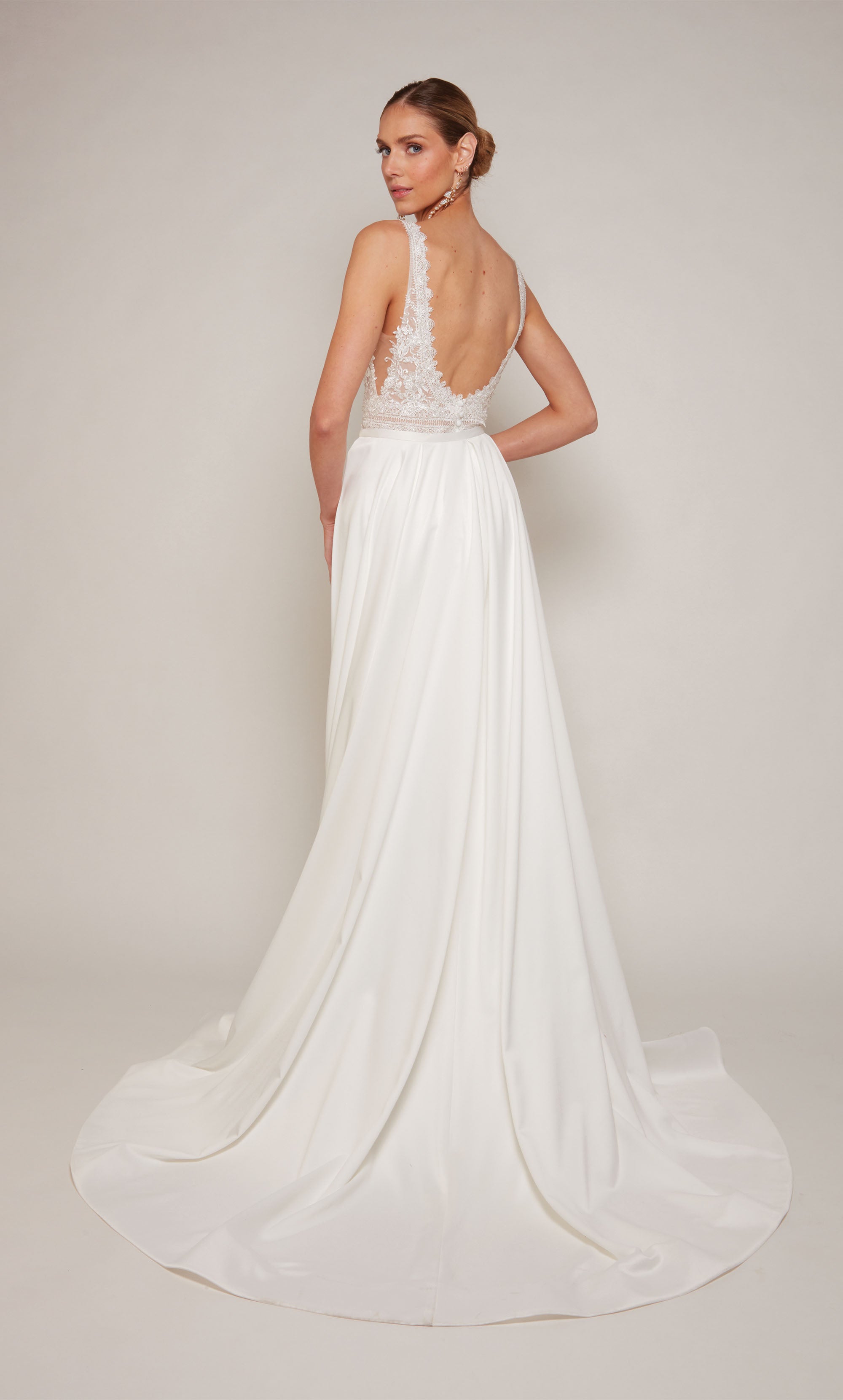 Luxurious satin sheath wedding dress in white with a V-neckline and delicate lace details. The dress comes with a detachable train that adds a hint of drama and formality during the ceremony, and can be detached for a more understated reception style.