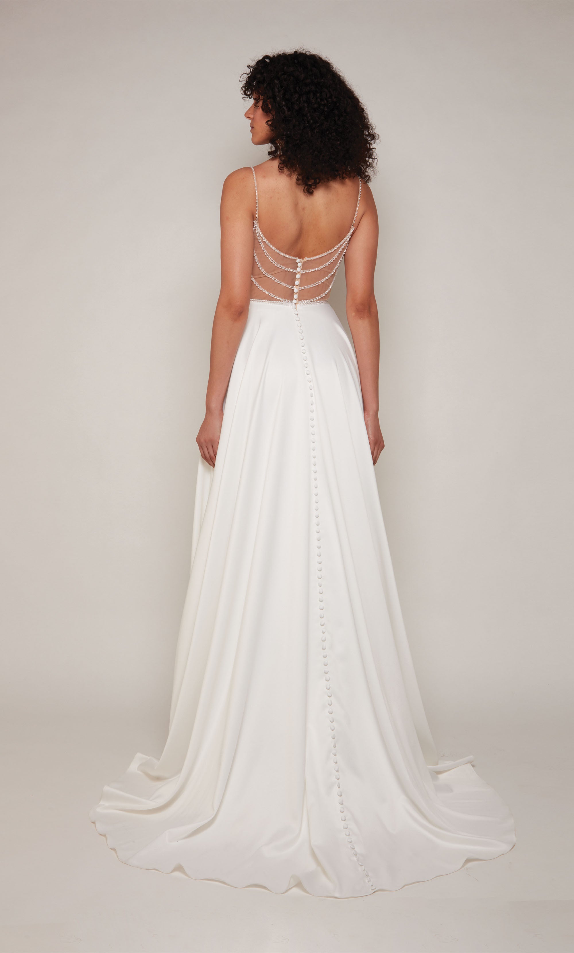 A classic, satin A-line wedding dress featuring a semi-sweetheart neckline and pearl embellishments on the straps, at the waistline, and on the illusion back. The dress also has an elegant train with satin-covered buttons down the back.